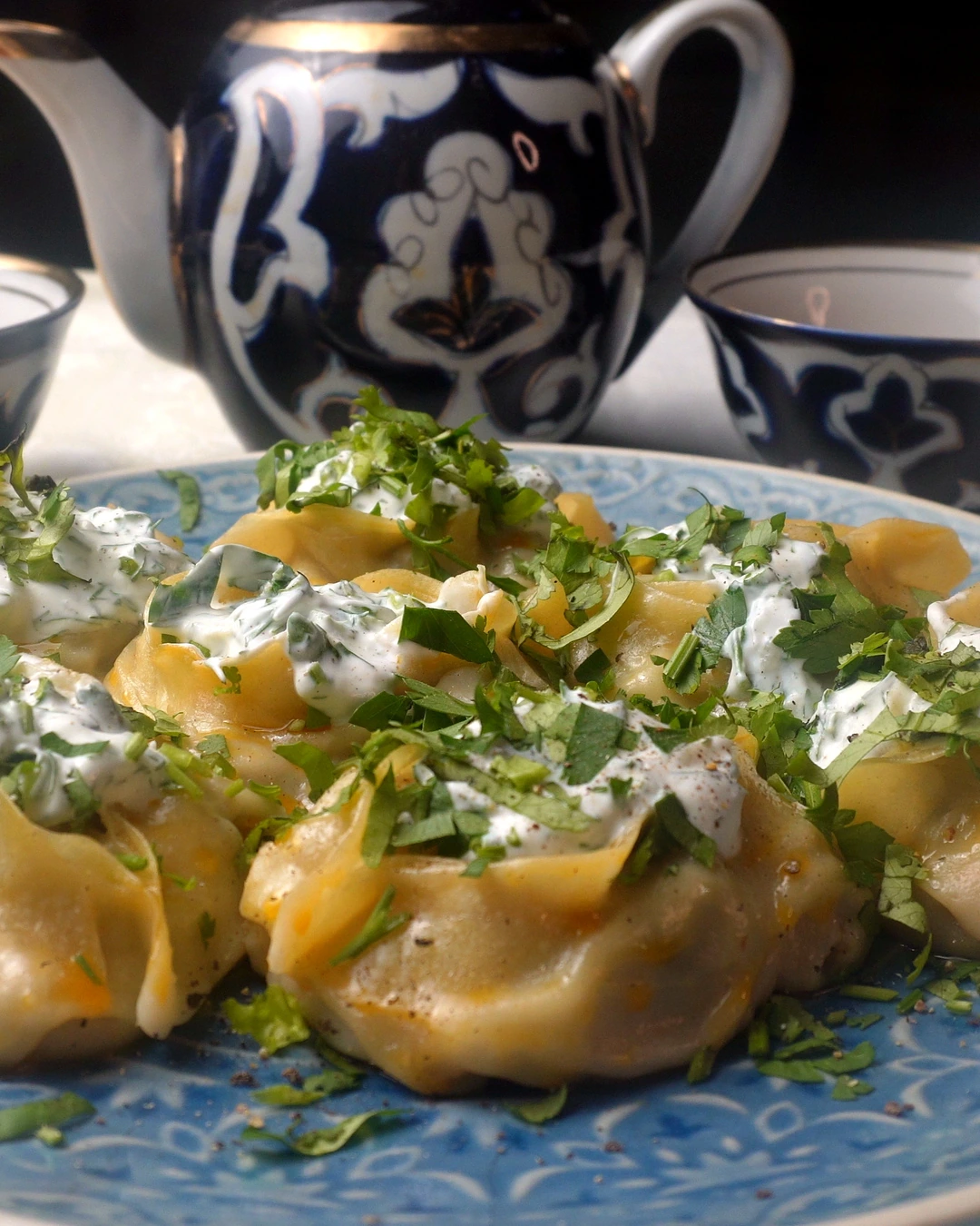 Steamed manti with herb sauce on a blue platter